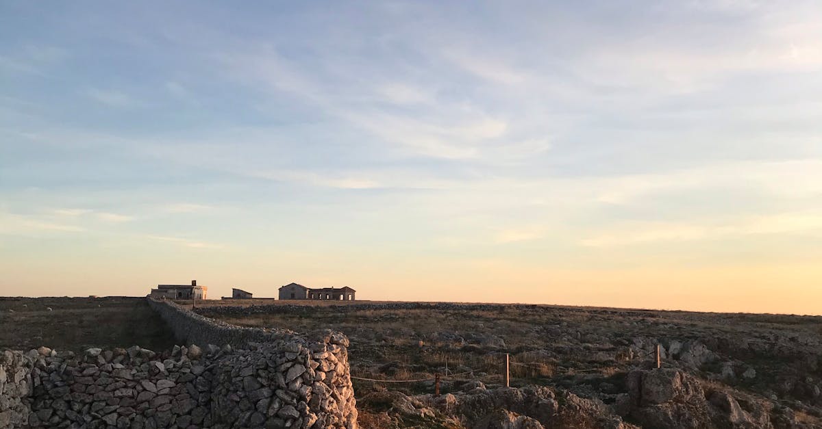 Weathered stone walls located on grassy ground with pebbles against cloudy sky and aged structures in rural area in evening time