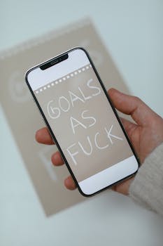 Hand holding smartphone displaying bold motivational text, emphasizing goals.