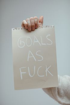 Hand holding a motivational poster with bold text on a gray background.