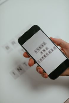 A hand holding a smartphone displaying tiles with the phrase 'Break the Internet' against a white background.