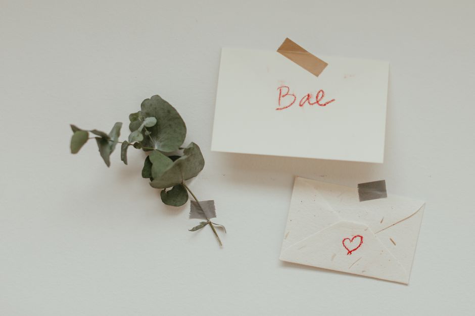 Minimalist composition with envelopes, leaves, and heart symbol on white background.