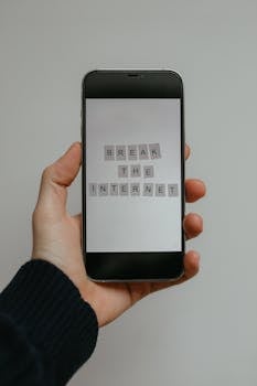 Close-up of a hand holding a smartphone displaying 'Break the Internet' on a gray background.