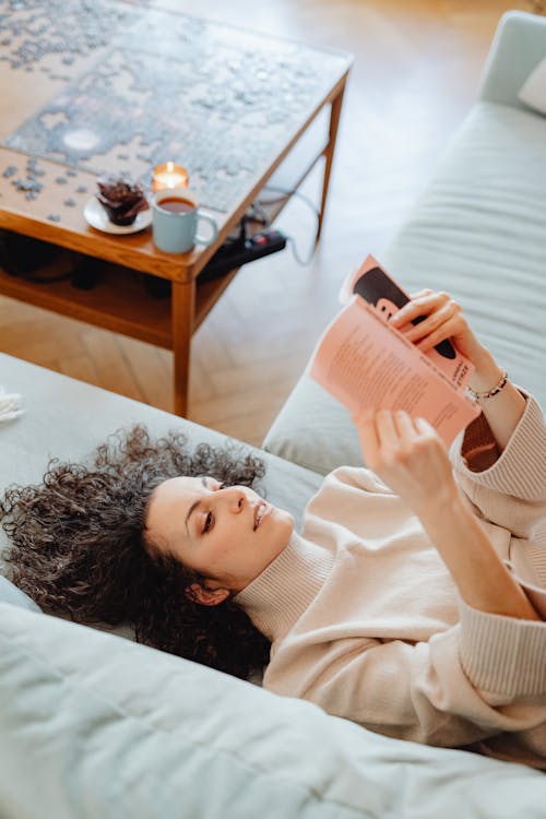 Woman in Turtle Neck Sweater Lying on a Couch while Reading a Book