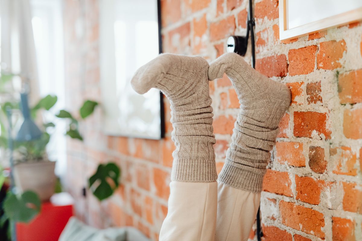 Feet in cozy grey knit boot socks resting against a brick wall