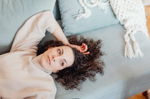 Woman in Turtle Neck Sweater Lying Near the Throw Pillows while Looking Afar
