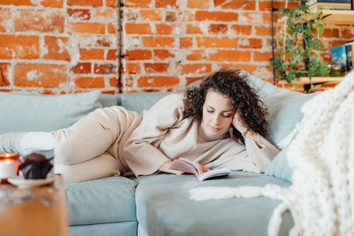 Free Woman Lying on a Couch while Reading a Book Stock Photo
