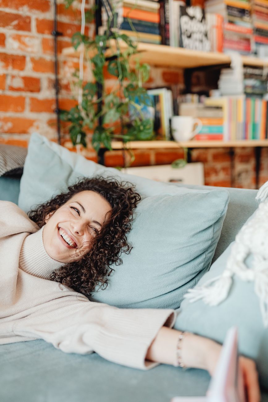 Smiling woman enjoying relaxing time on a cozy sofa in a stylish home setting.