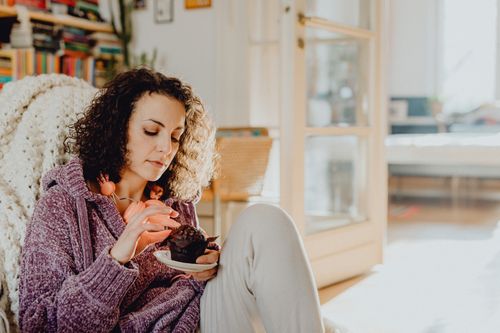 Free Woman with curly hair enjoying a cupcake in a cozy living room setting. Stock Photo