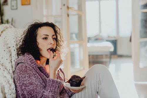 Free Woman in a cozy sweater eating a muffin indoors, enjoying a relaxed moment. Stock Photo