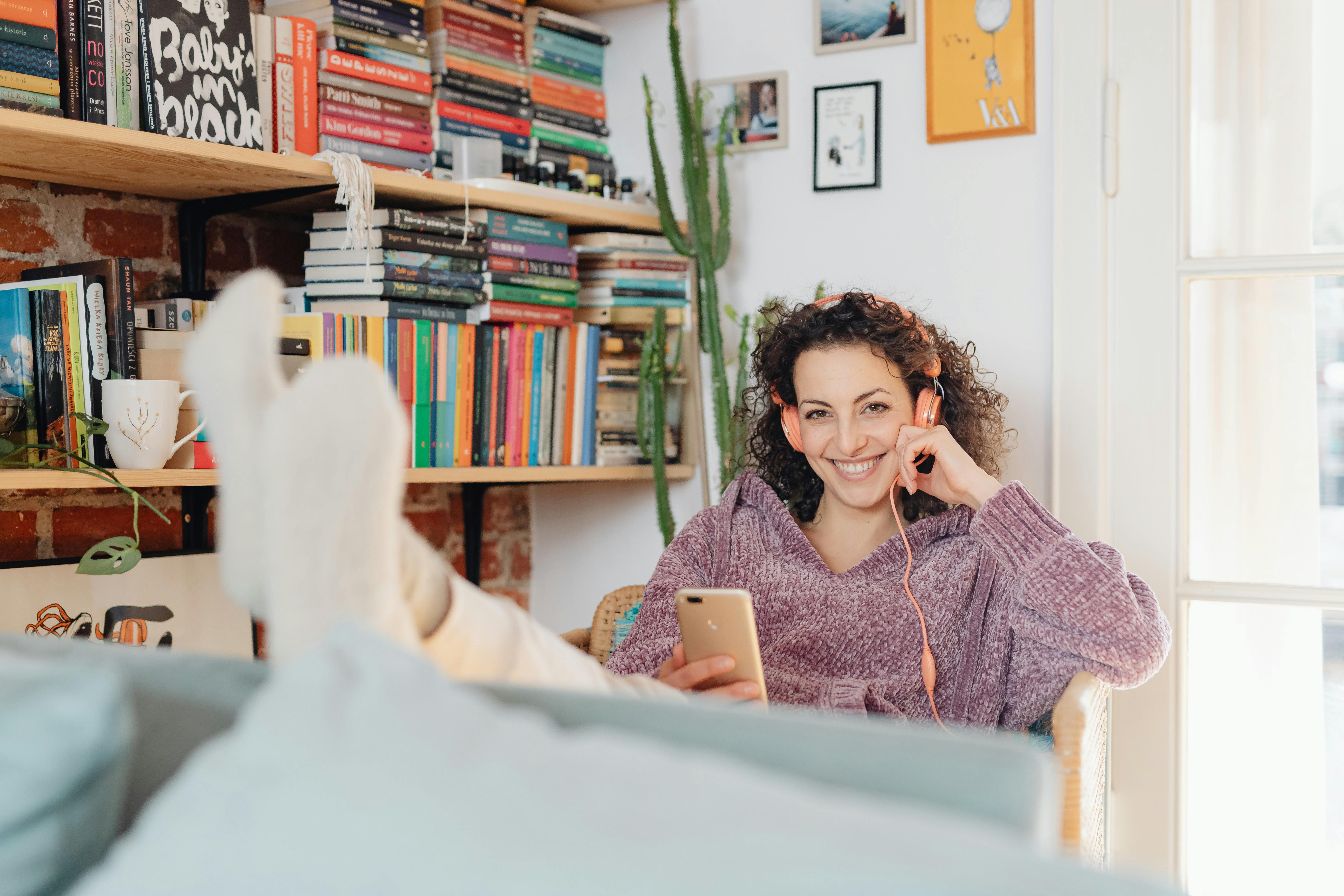 Woman relaxing with music in a cozy book-filled corner at home.