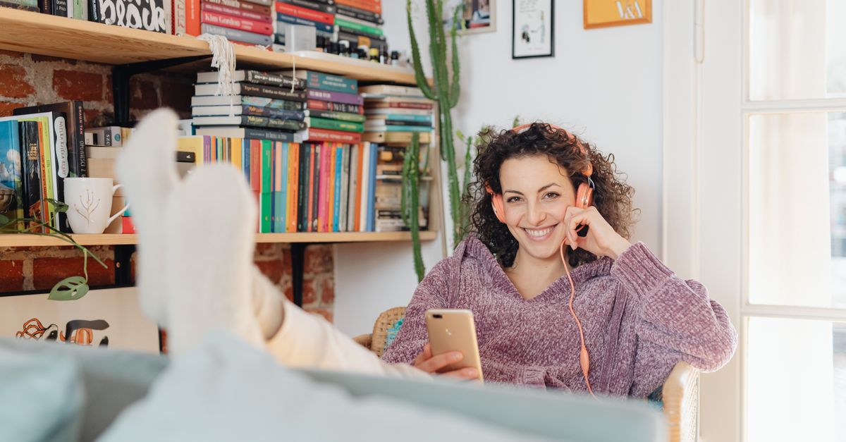 A person sitting in a cozy chair, surrounded by books and plants, looking thoughtfully at a phone
