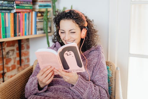 Free Portrait of a Smiling Woman Wearing Headphones and Reading a Book Stock Photo