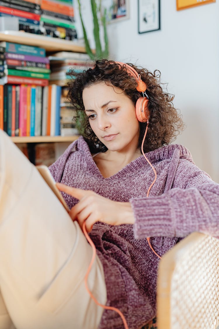 Woman Reading A Book At Home While Listening To Music On Headphones 