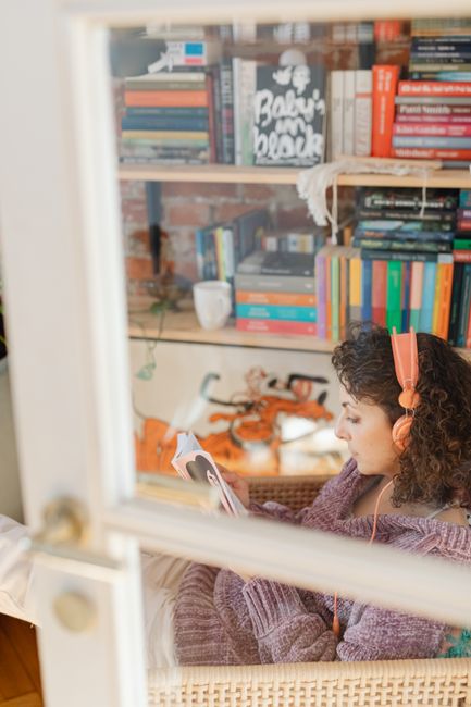 Woman relaxing with a book and headphones beside a bookshelf, the cadence of audiobook listening that fits a long planning year.