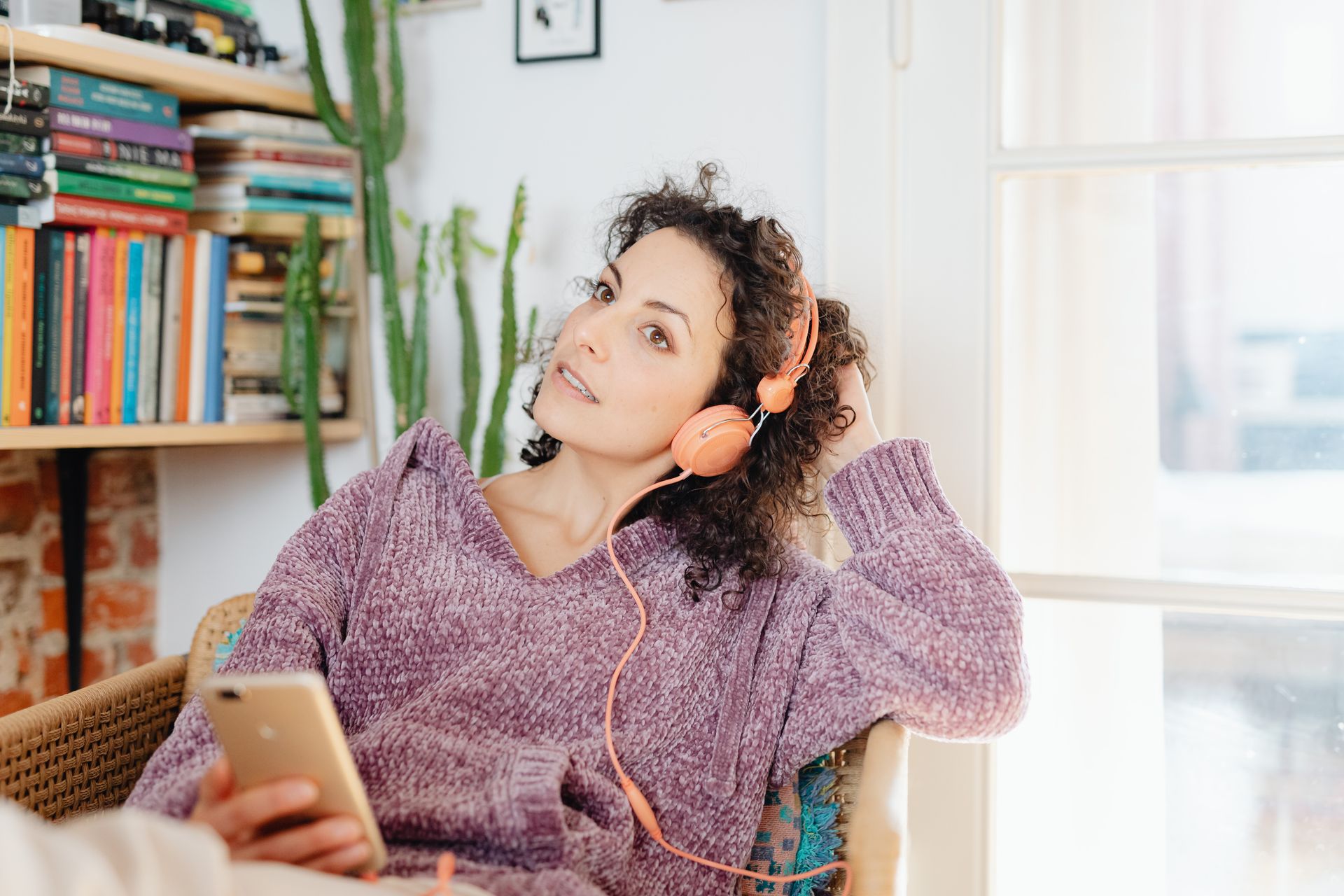 Caucasian woman in a cozy setting listening to music through headphones while using a smartphone.