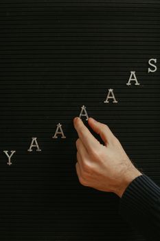 Close-up of a hand placing letters on a black letter board with a diagonal pattern.