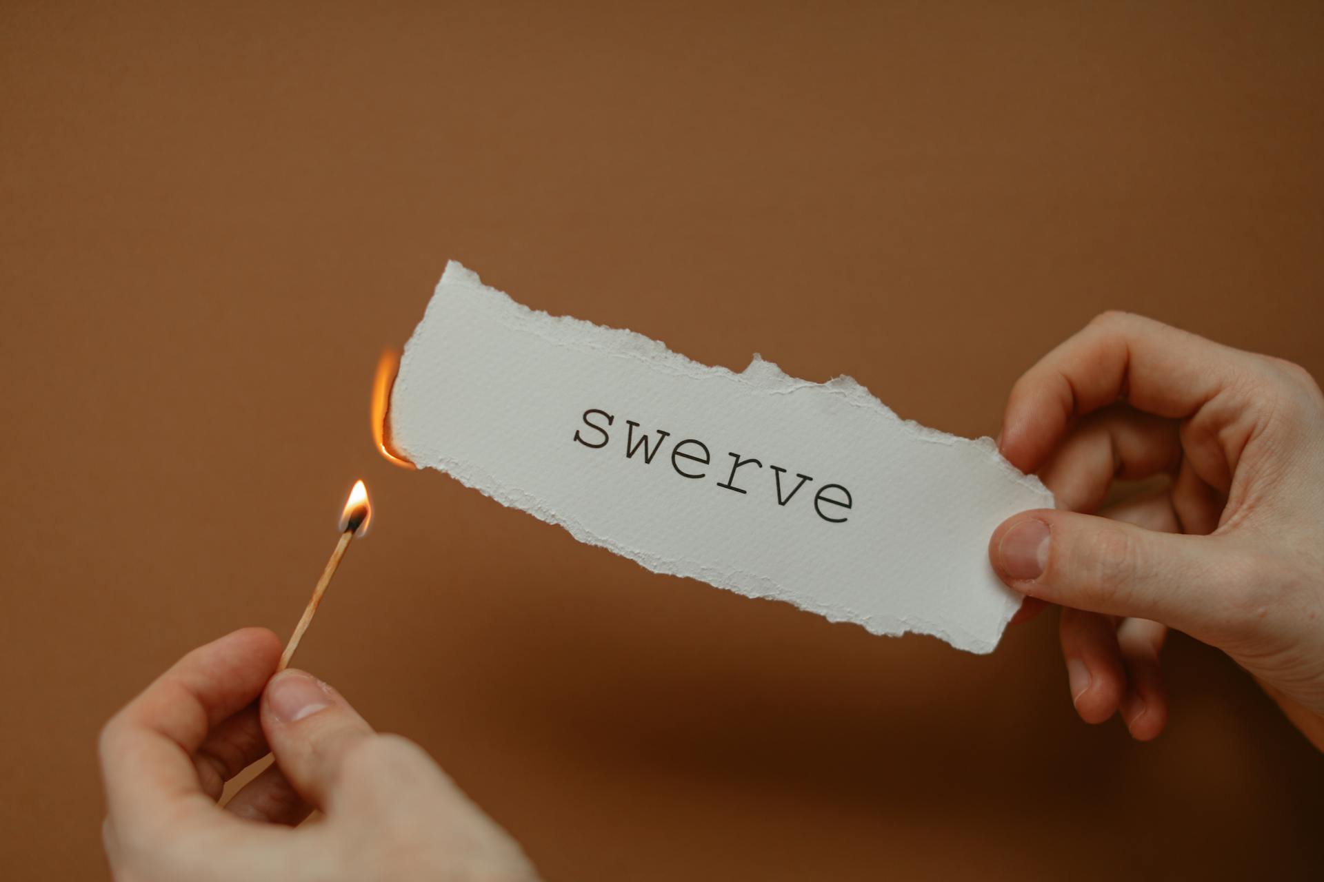 Close-up of hands holding burning paper with 'swerve', symbolizing change or danger.