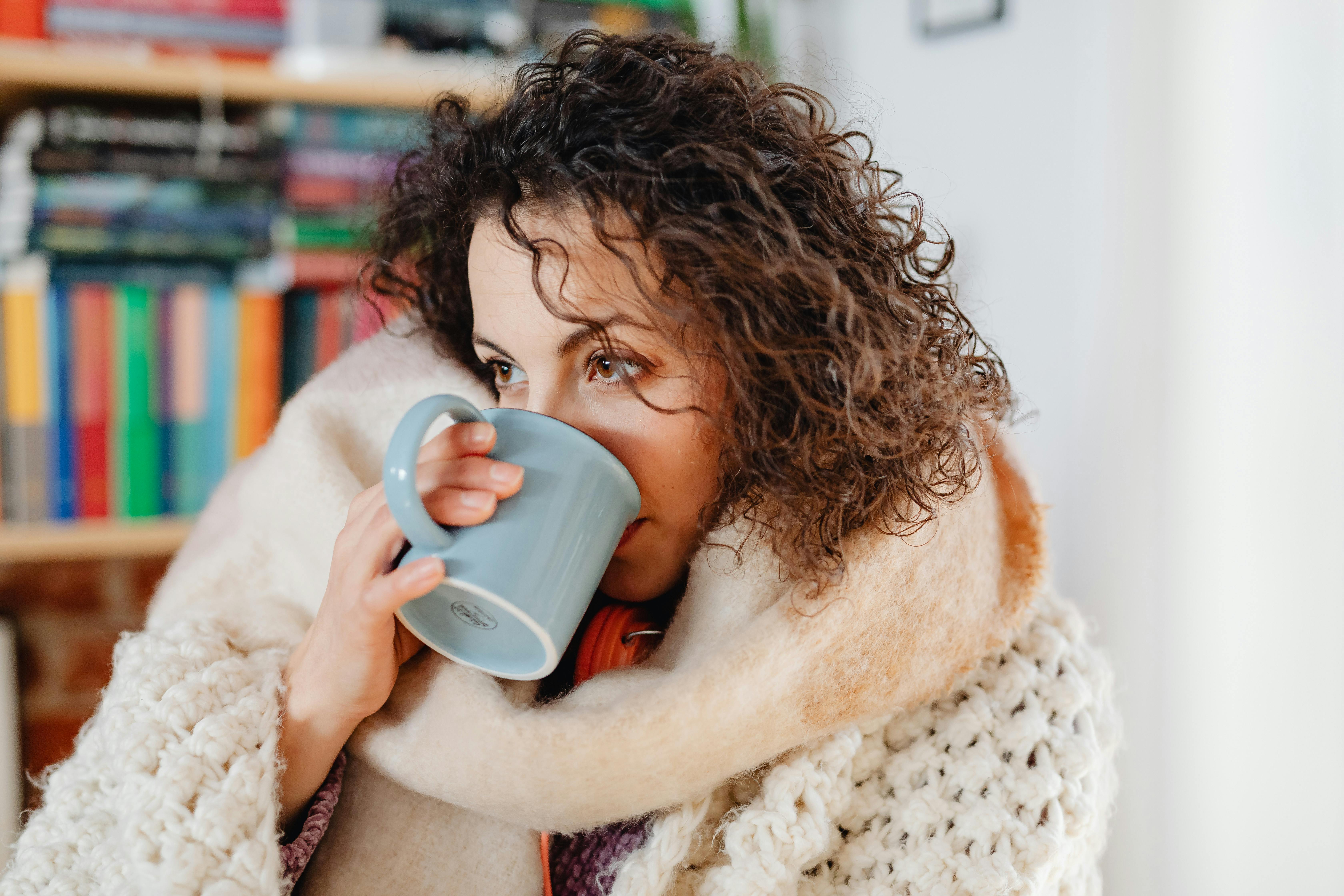 Photo of a Woman Wearing a Scarf Drinking from a Blue Mug