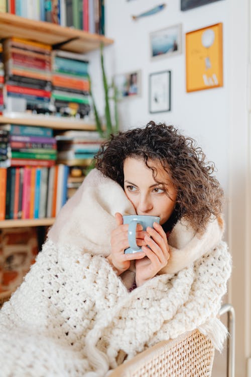 Woman Holding a Blue Mug with a White Knitted Blanket Around Her Body