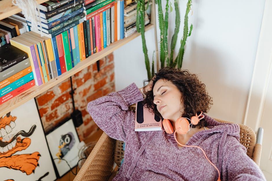 Calm vs Headspace: Sleep Meditation Effectiveness Showdown (2024) A Caucasian woman with curly hair relaxes at home in a cozy chair, holding a book with headphones.