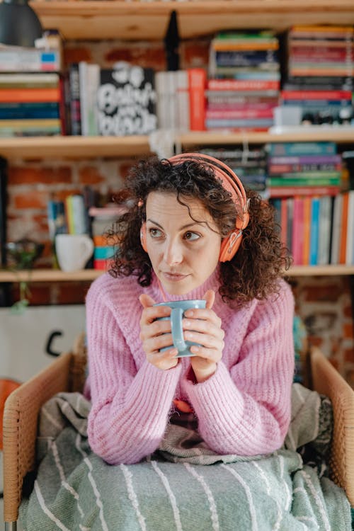 Free Woman in a Pink Knitted Sweater Holding a Blue Mug while Looking Away Stock Photo