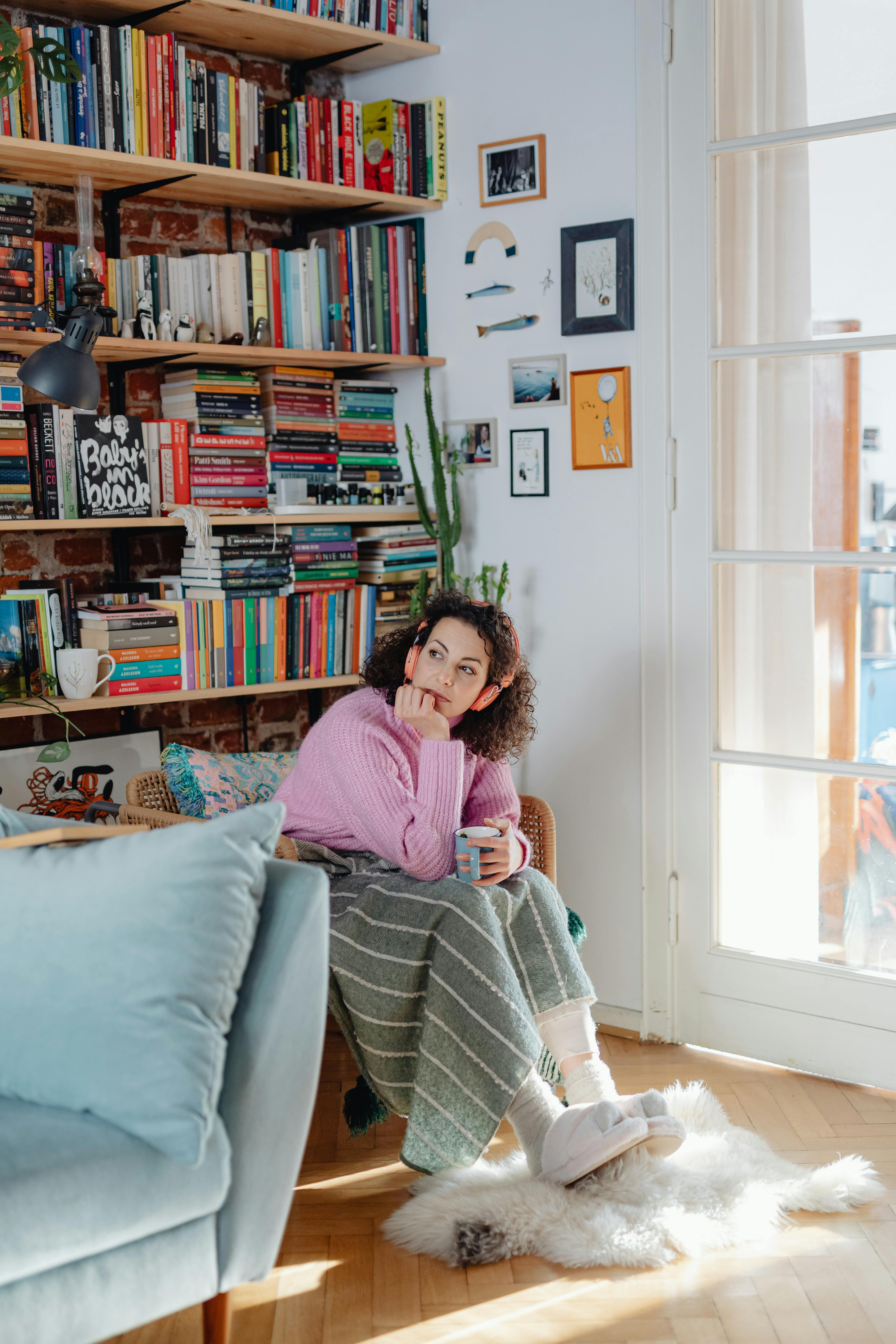 Free Woman in a cozy living room with books and blankets, enjoying a quiet moment. Stock Photo