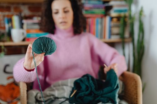 Free A woman in a pink sweater focuses on knitting with yarn in a cozy home environment. Stock Photo