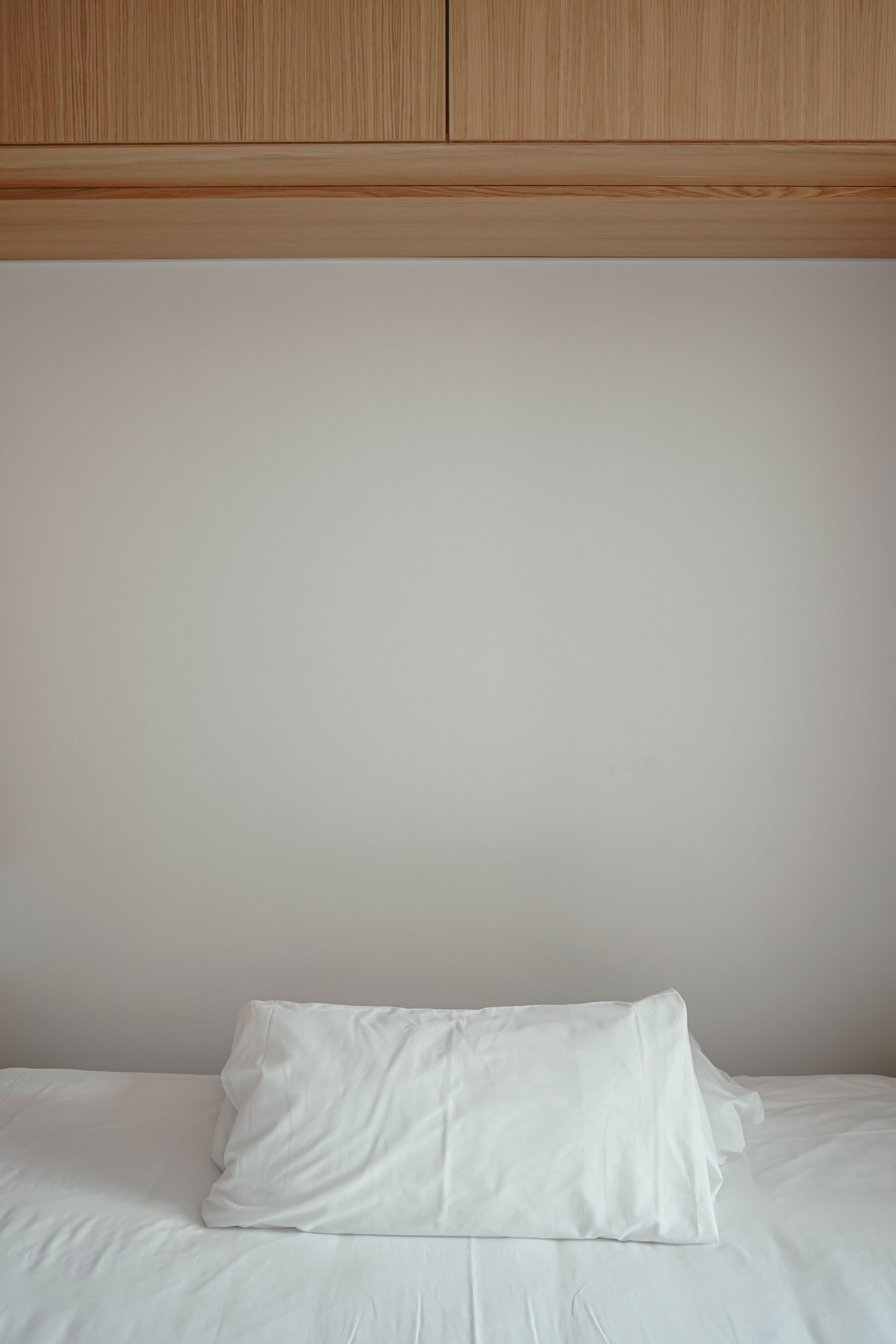 A simple and serene bedroom setup with a white bed and wooden cabinet.