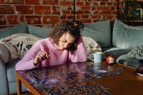 Free A woman enjoys assembling a jigsaw puzzle in a cozy, sunlit living room. Stock Photo