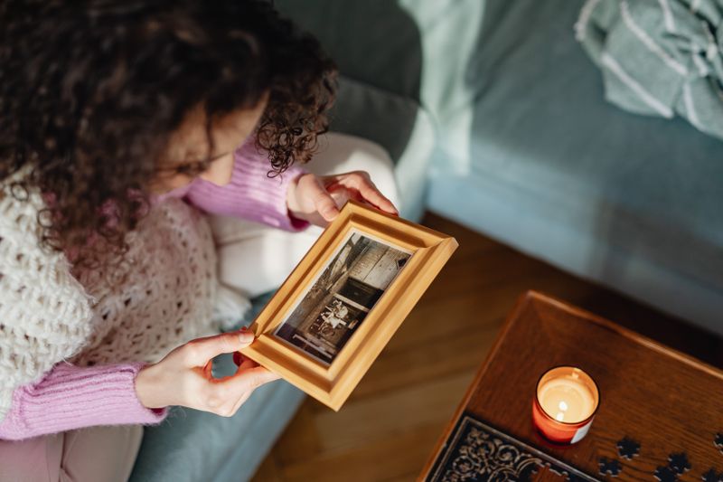 High angle view of a woman looking at a framed sepia photograph and a candle on a table representing quiet memory and reflection
