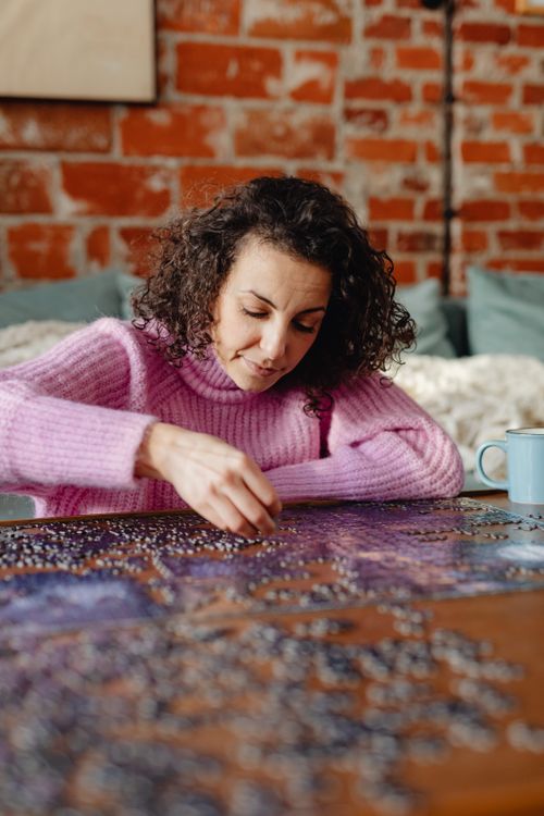 Free A woman enjoying leisure time indoors, working on a jigsaw puzzle with a cozy atmosphere. Stock Photo
