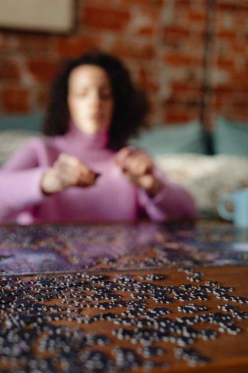Free A woman in focus placing pieces of a puzzle on a table, enjoying a leisure activity indoors. Stock Photo