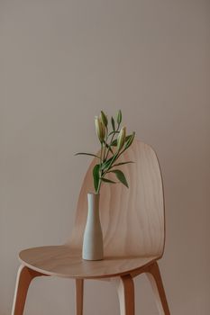 Elegant minimalist setup with a vase of flowers on a wooden chair against a neutral backdrop.
