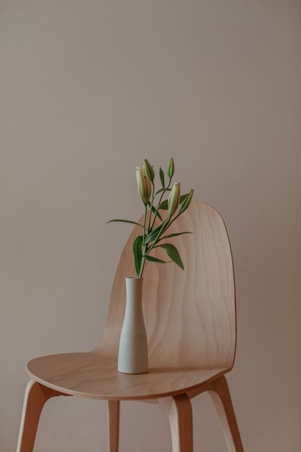 Elegant minimalist setup with a vase of flowers on a wooden chair against a neutral backdrop.