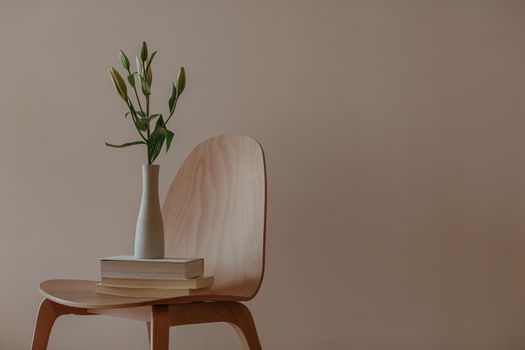 A minimalist setup with a wooden chair, vase, and stack of books indoors.