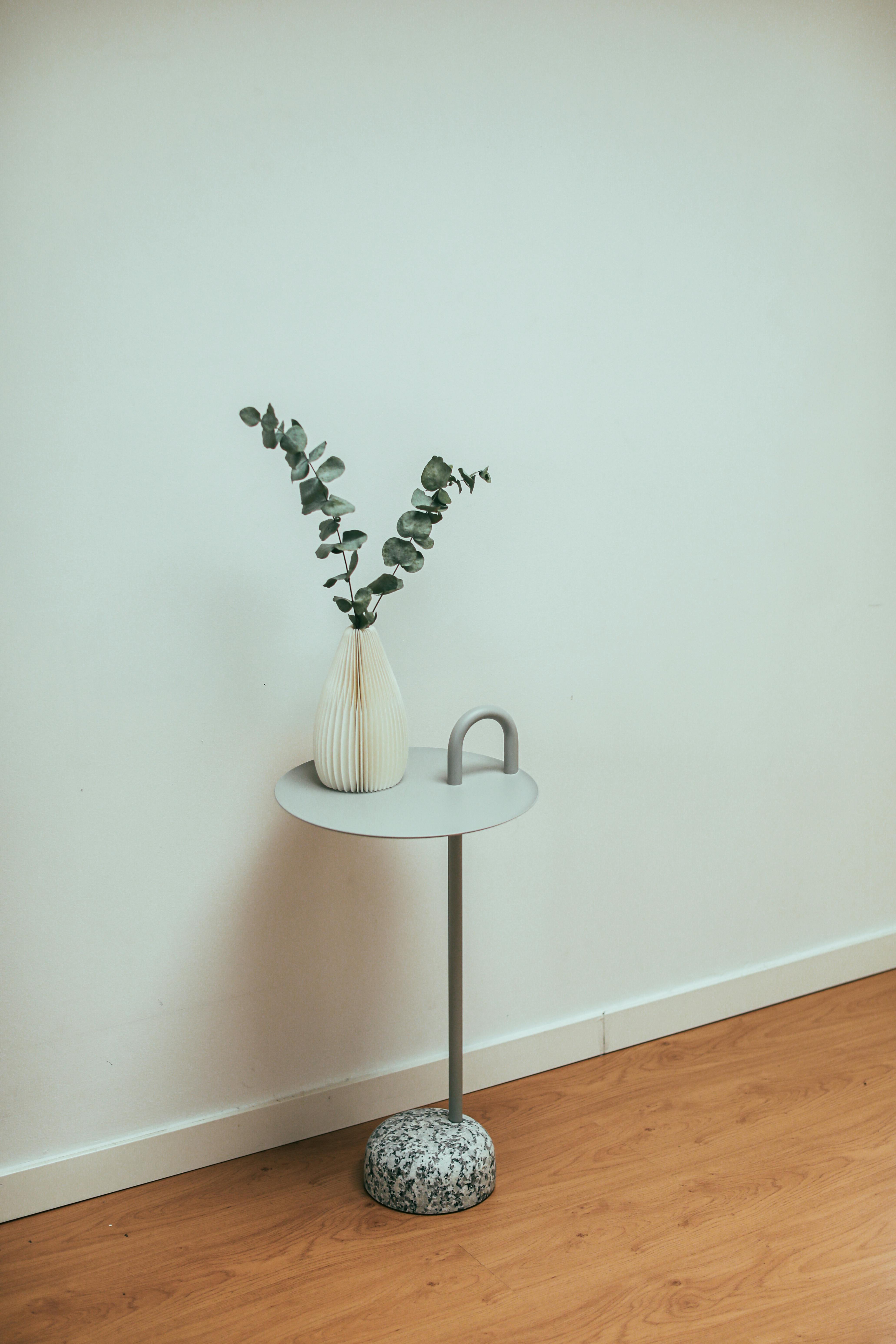 Simple and elegant scene featuring a white vase with eucalyptus branches on a modern table against a plain wall.