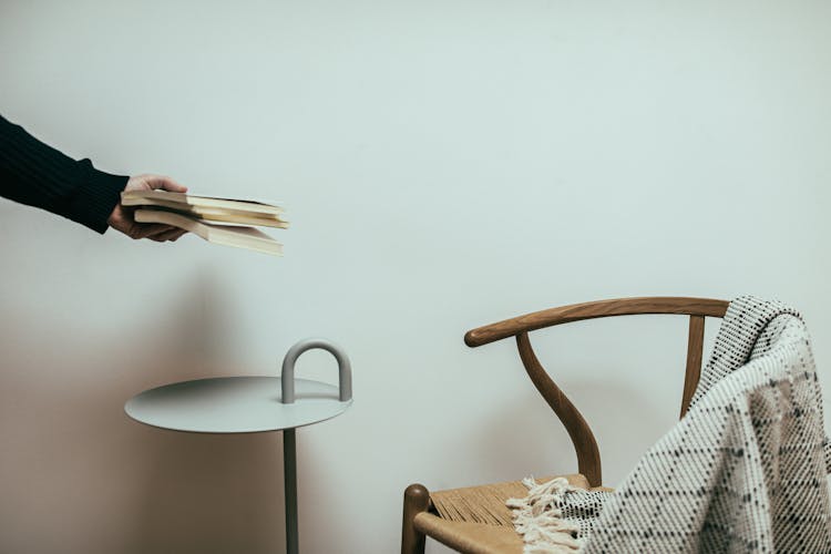 Person Holding Books Beside A Side Table