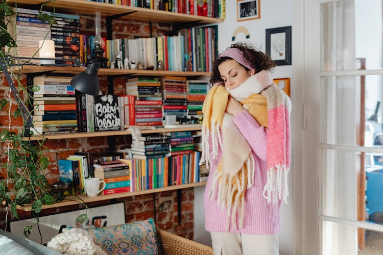 Woman In A Warm Pastel Scarf And Pink Sweater Standing In A Living Room 