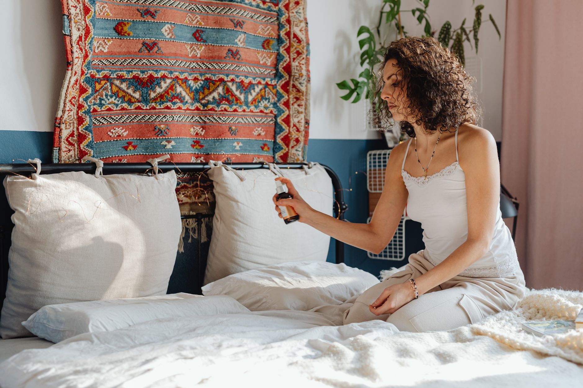 A young woman sitting on a bed in a cozy bedroom, using aromatherapy spray for relaxation.