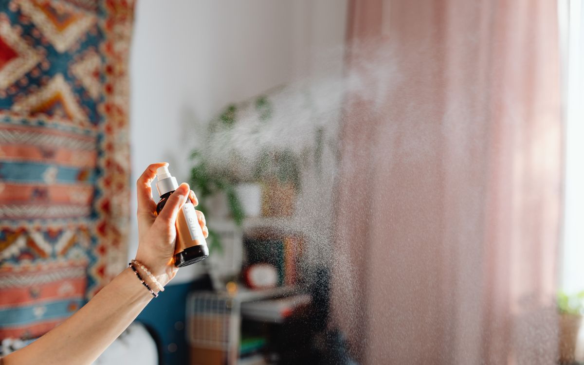 A hand spraying room freshener in a cozy home interior with ethnic decor and natural light.
