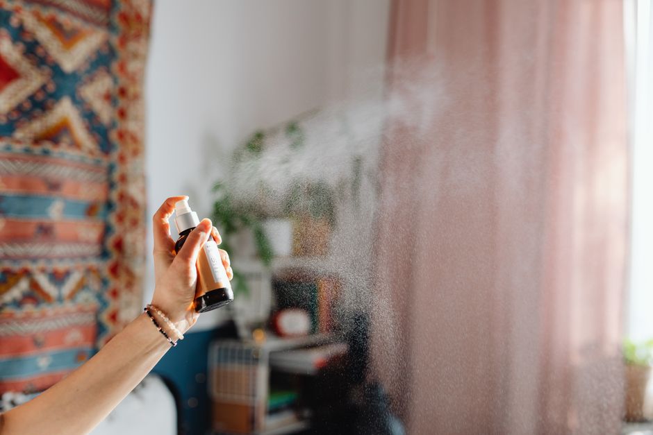 A hand spraying room freshener in a cozy home interior with ethnic decor and natural light.