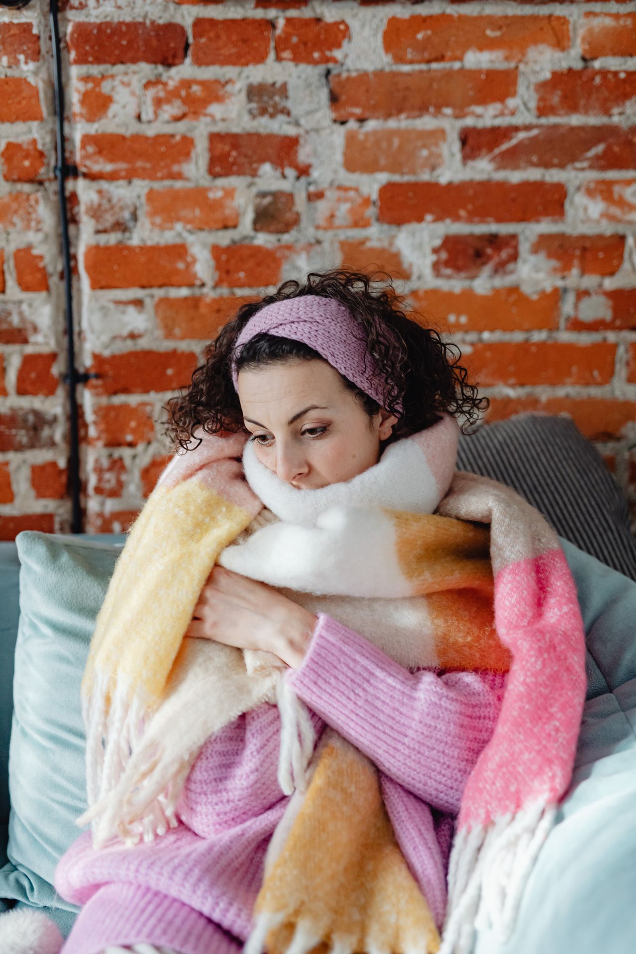 Woman wrapped in a chunky pink and yellow knit scarf indoors