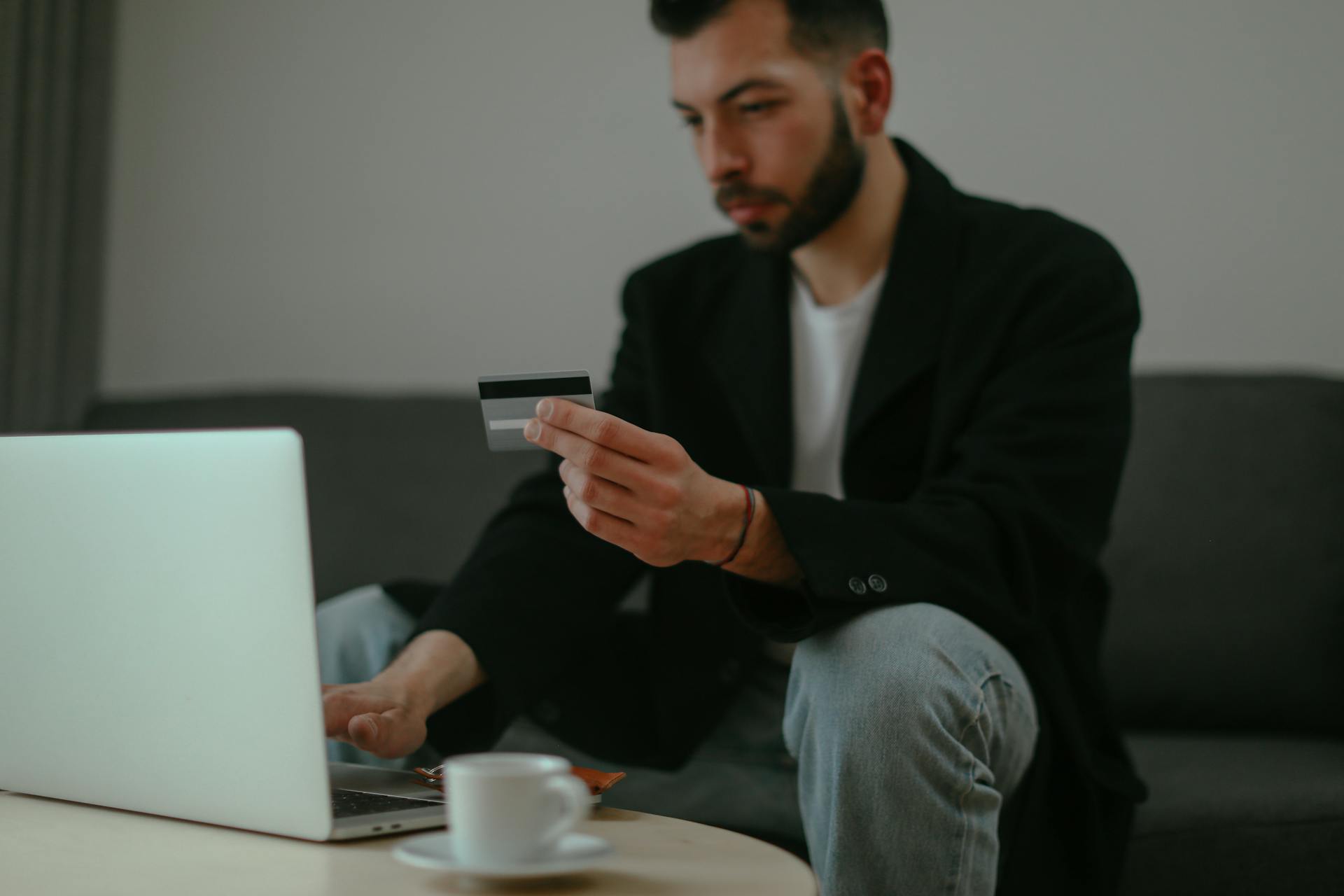 Focused man holding a credit card while shopping online with a laptop in an indoor setting.