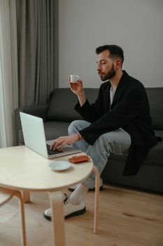 Man sitting on a couch using a laptop while holding a coffee cup in a cozy home setting.