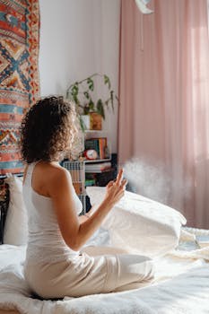 A woman sits on her bed, spraying sanitizer on a pillow in a cozy and well-decorated bedroom.
