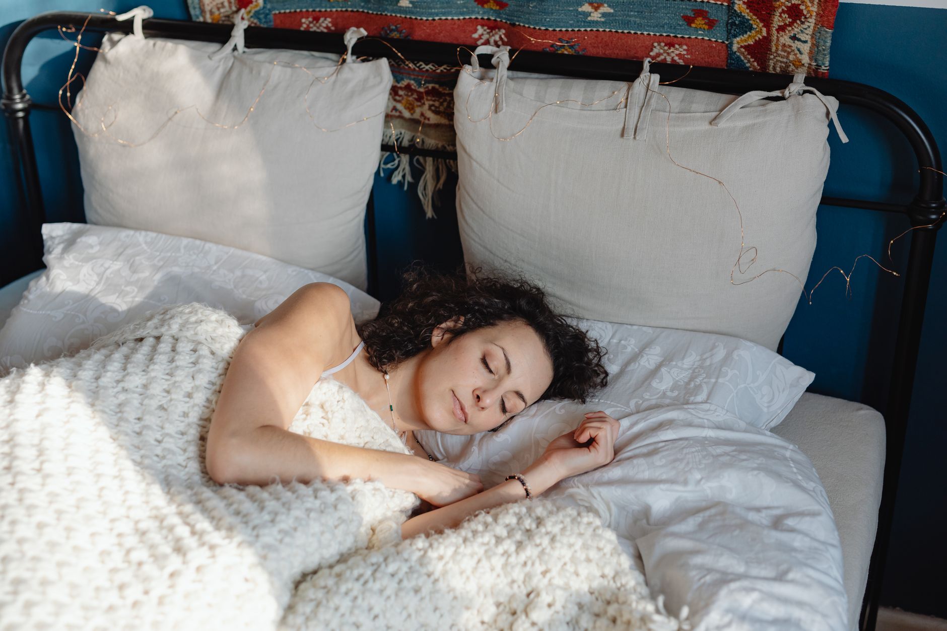A woman sleeping under a textured blanket, capturing the tactile reassurance that natural-fibre sleep products promise.
