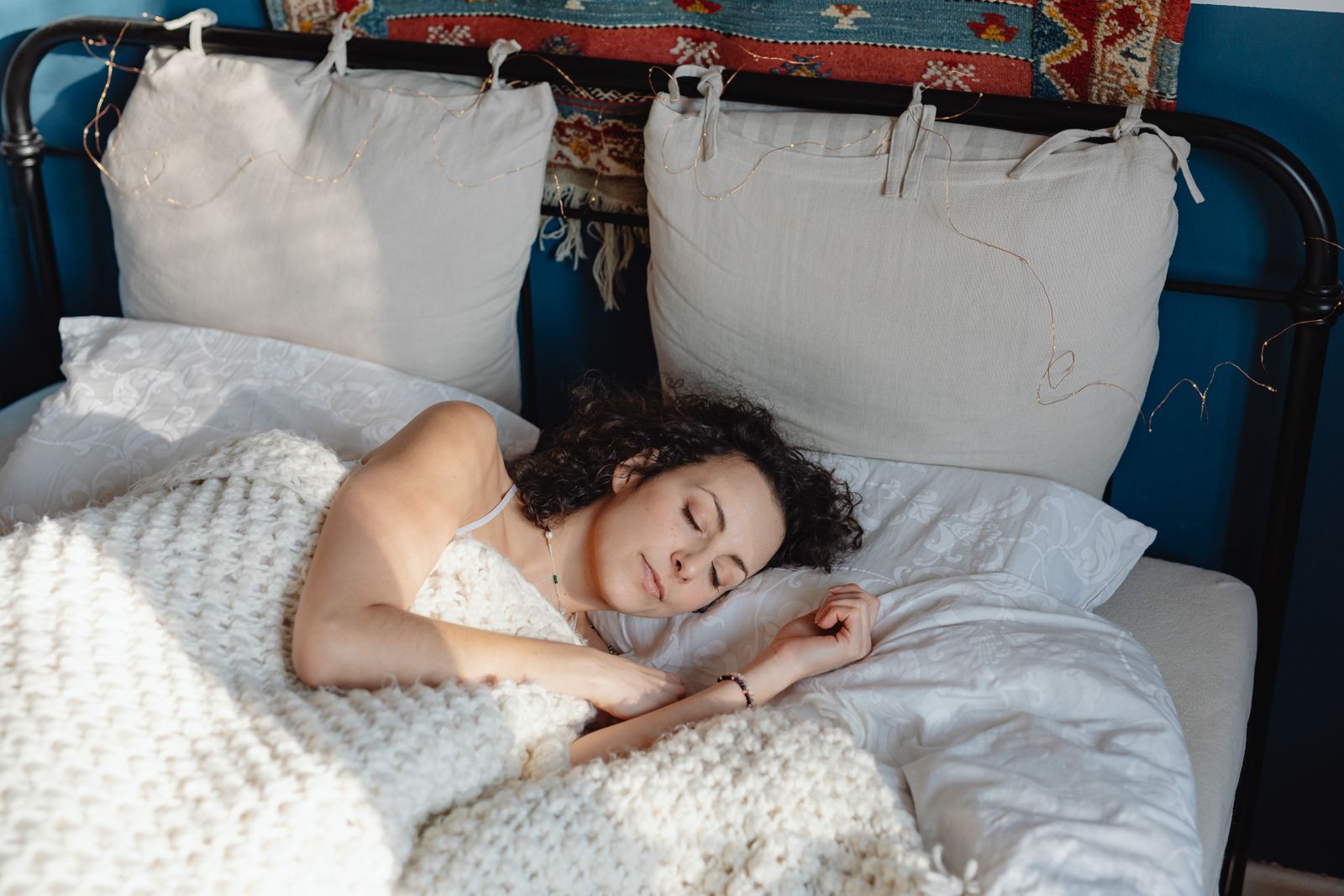 A young woman with curly hair sleeping peacefully in a cozy bed with knitted blankets.