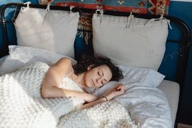 A young woman with curly hair sleeping peacefully in a cozy bed with knitted blankets.