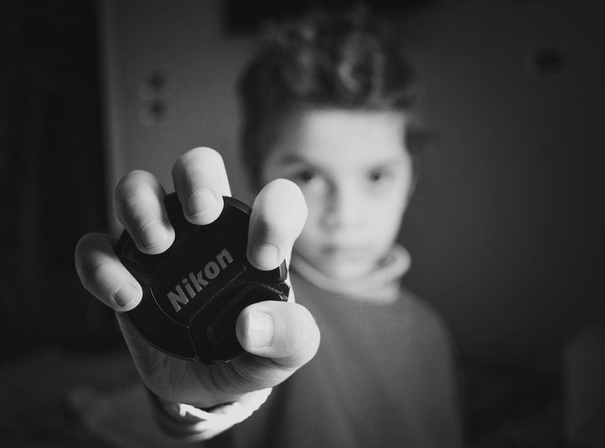 A young boy presenting a Nikon lens cap, captured in a dramatic black and white portrait.