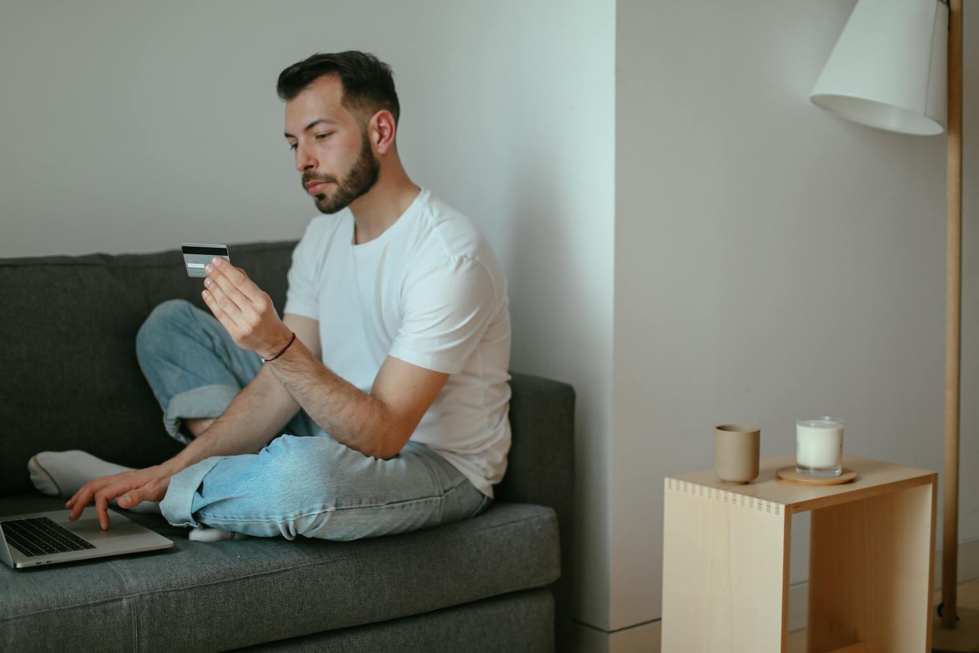 Adult male sitting on couch shopping online with a laptop and credit card.